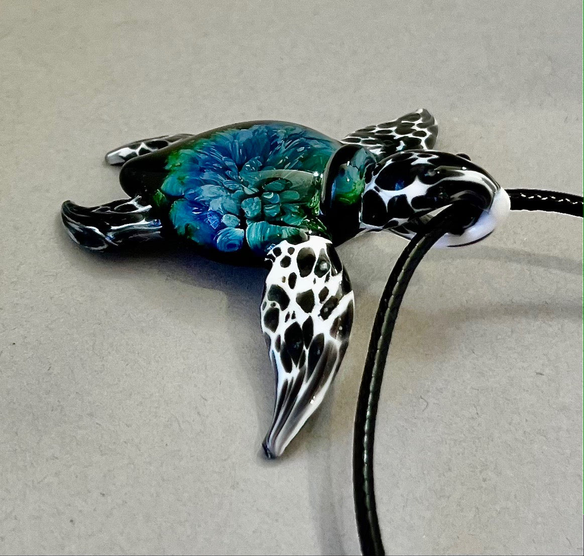 glass black and white spotted sea turtle pendant with iceberg style explosion in the shell at a 360 degree angle.